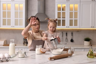 Photo of Tired housewife cooking with her little daughter at marble table in kitchen