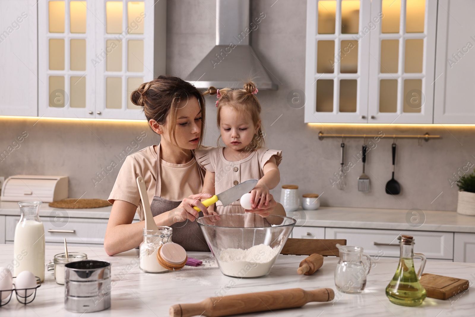 Photo of Housewife cooking with her little daughter at marble table in kitchen