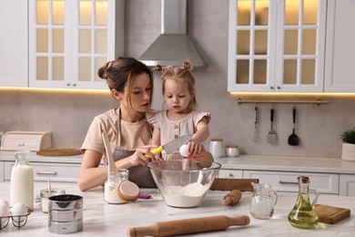 Housewife cooking with her little daughter at marble table in kitchen