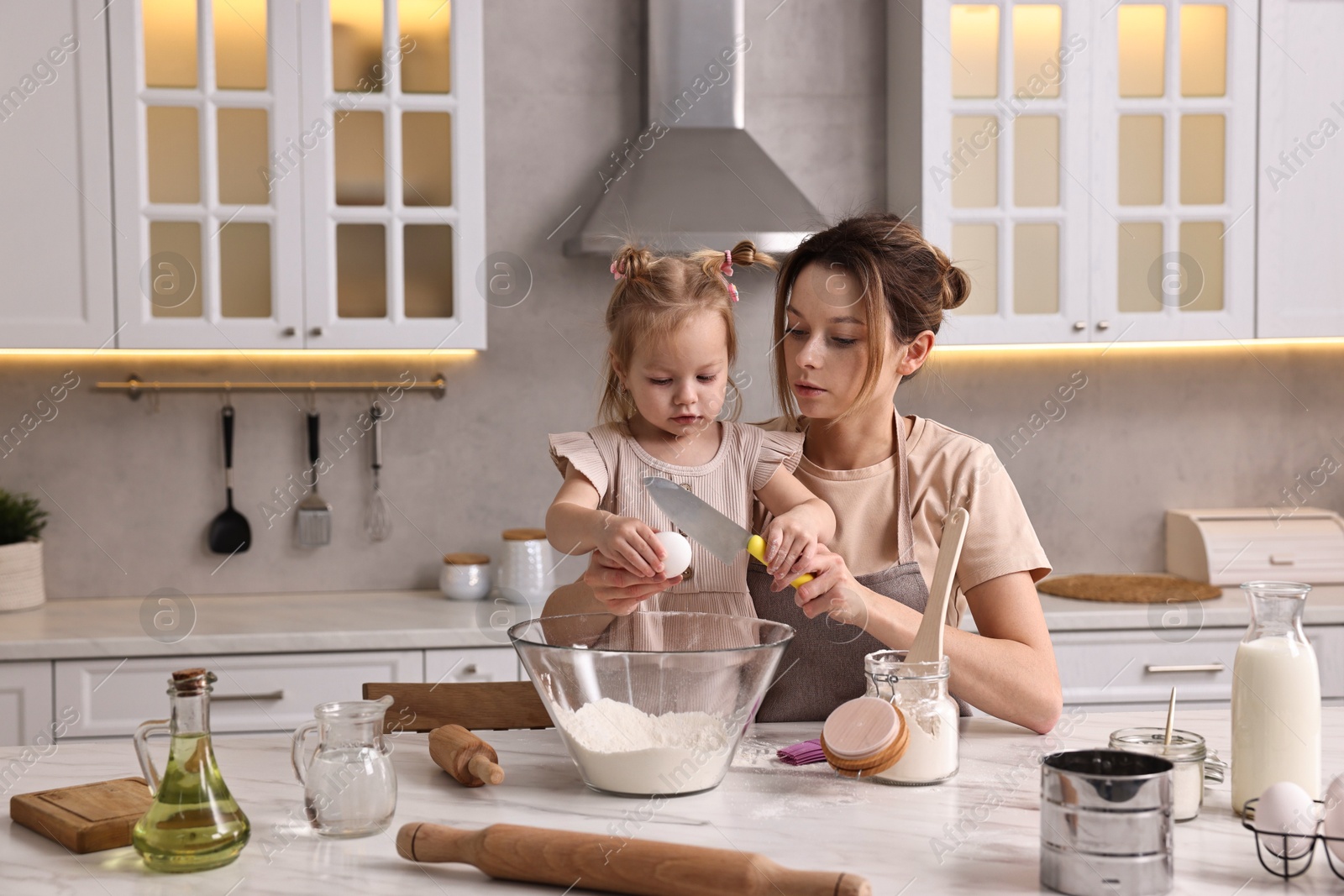 Photo of Housewife cooking with her little daughter at marble table in kitchen