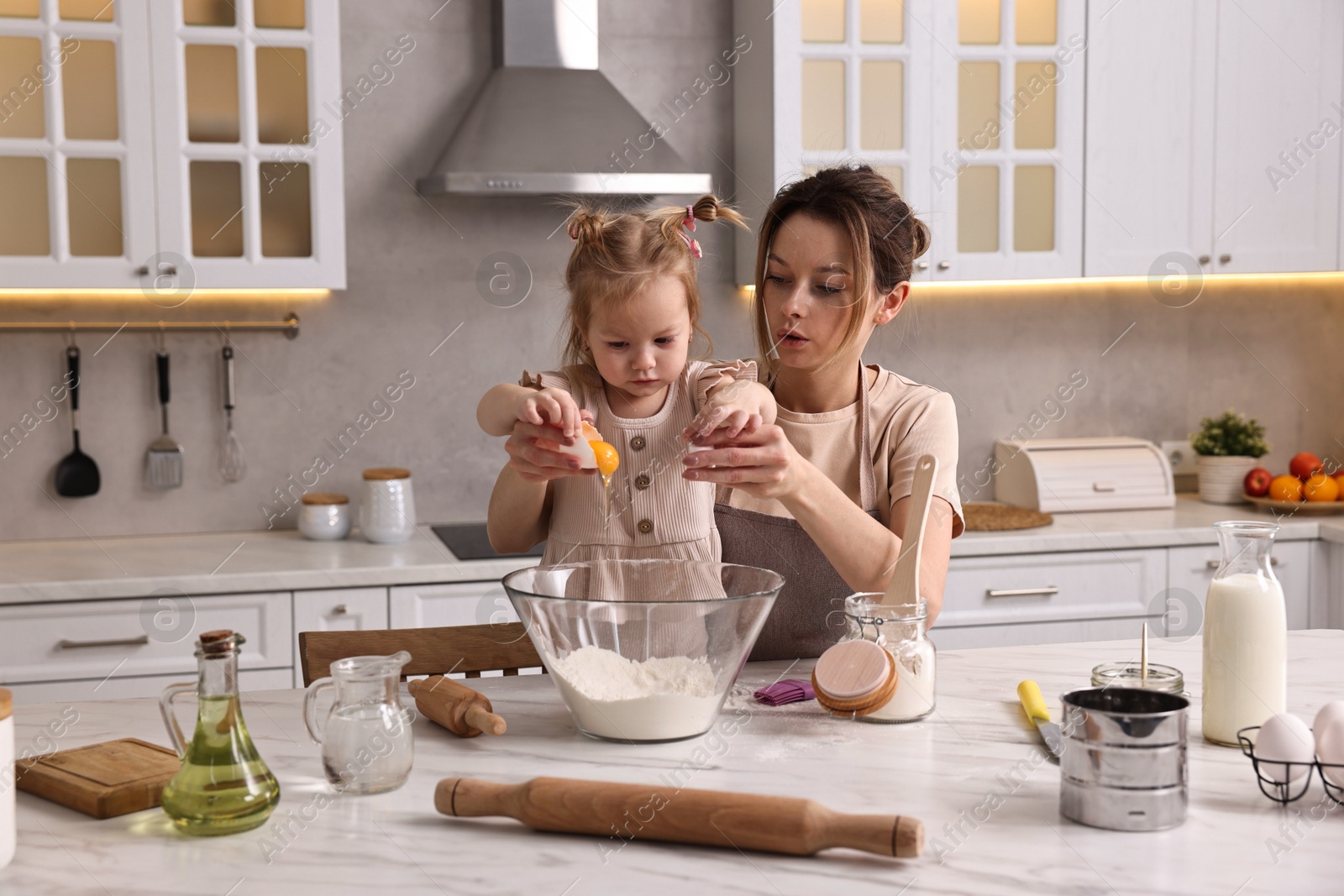 Photo of Housewife cooking with her little daughter at marble table in kitchen