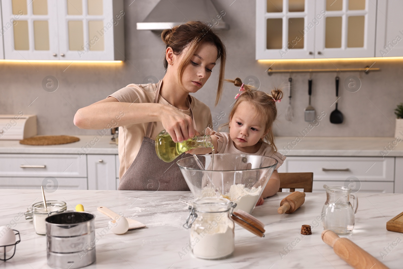 Photo of Housewife cooking with her little daughter at marble table in kitchen