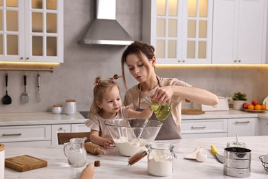 Housewife cooking with her little daughter at marble table in kitchen