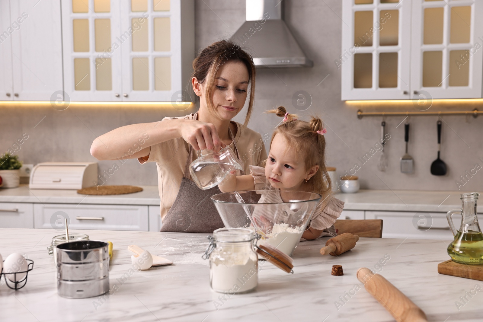 Photo of Housewife cooking with her little daughter at marble table in kitchen