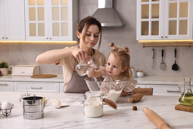 Housewife cooking with her little daughter at marble table in kitchen