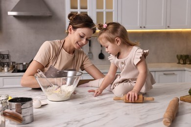 Smiling housewife cooking with her little daughter at marble table in kitchen