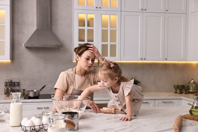 Tired housewife cooking with her little daughter at marble table in kitchen