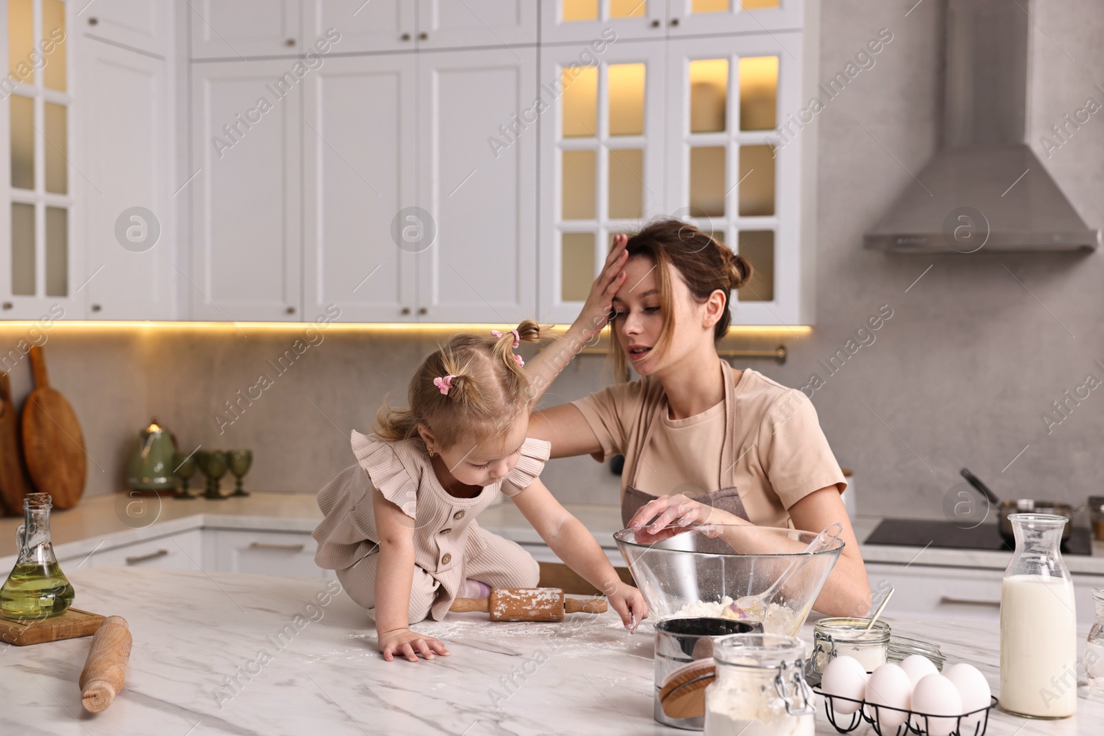 Photo of Tired housewife cooking with her little daughter at marble table in kitchen