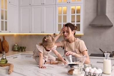 Tired housewife cooking with her little daughter at marble table in kitchen