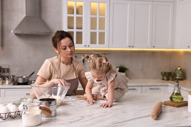 Photo of Tired housewife cooking with her little daughter at marble table in kitchen