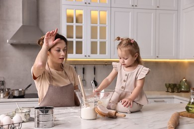 Tired housewife cooking with her little daughter at marble table in kitchen