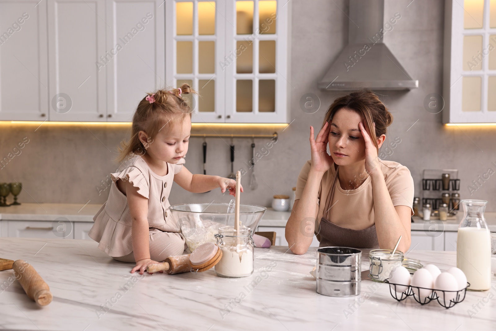 Photo of Tired housewife cooking with her little daughter at marble table in kitchen