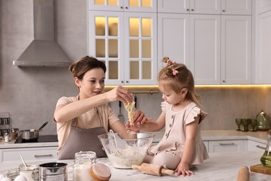 Smiling housewife cooking with her little daughter at marble table in kitchen