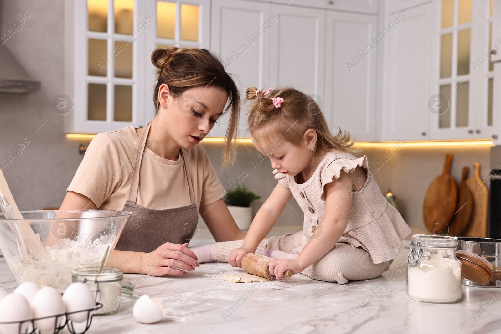 Photo of Housewife cooking with her little daughter at marble table in kitchen