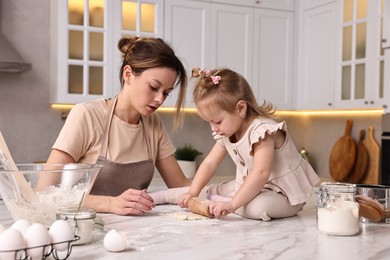 Housewife cooking with her little daughter at marble table in kitchen