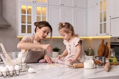 Housewife cooking with her little daughter at marble table in kitchen