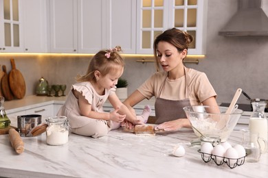 Photo of Housewife cooking with her little daughter at marble table in kitchen