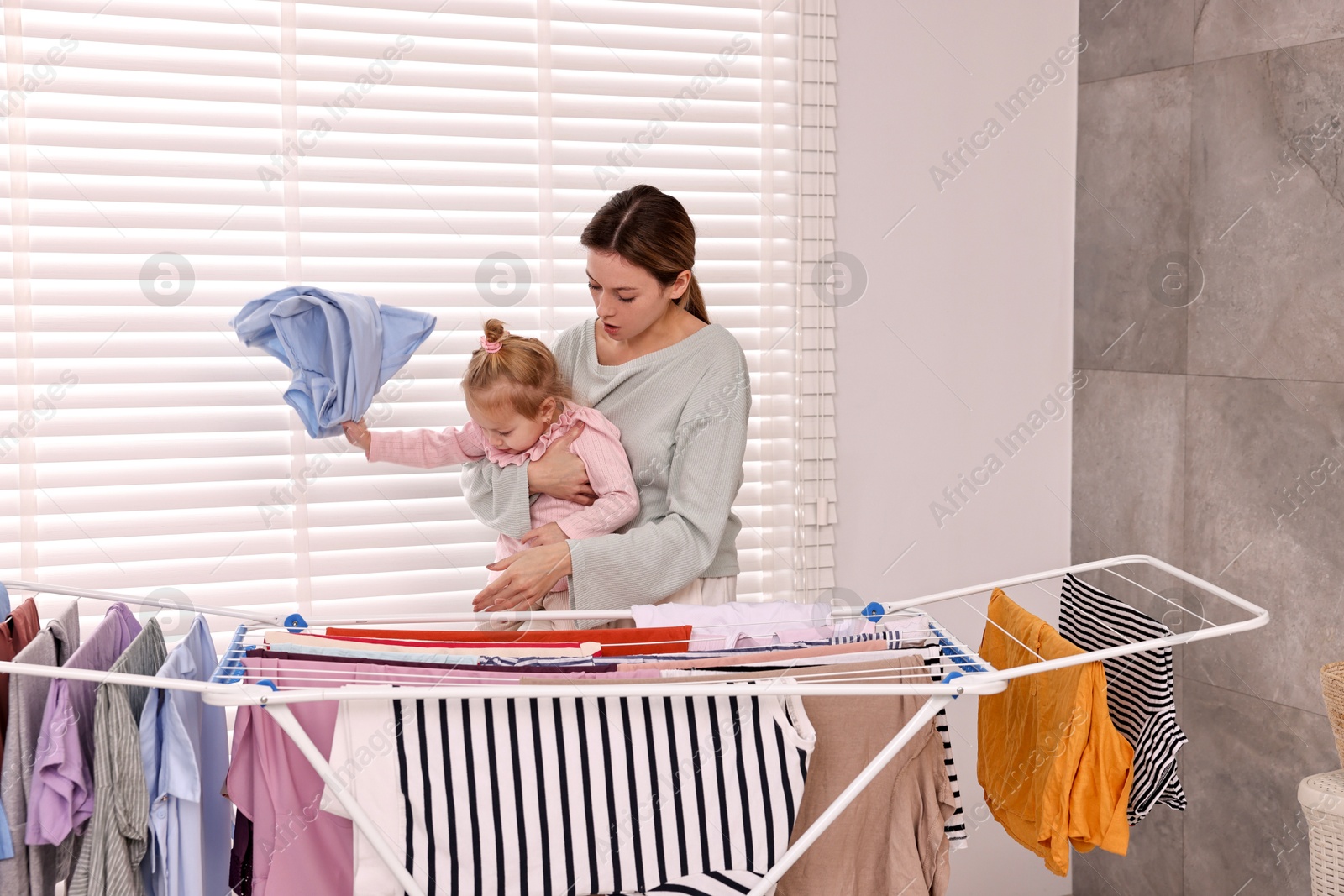 Photo of Housewife with her daughter hanging clothes on drying rack at home