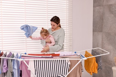 Housewife with her daughter hanging clothes on drying rack at home