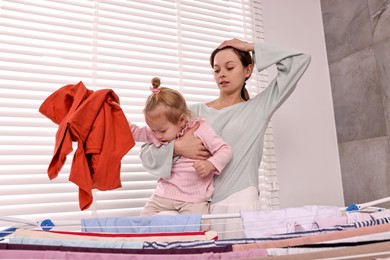 Photo of Housewife with her daughter hanging clothes on drying rack at home