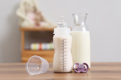 Photo of Milk in feeding bottle, jug and pacifier on wooden table indoors