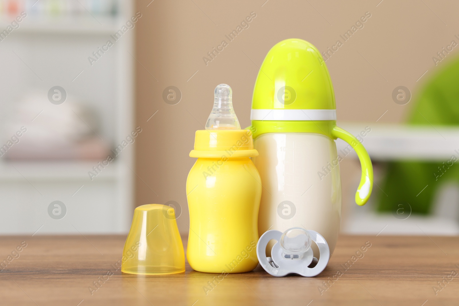 Photo of Feeding bottles with milk and pacifier on wooden table indoors