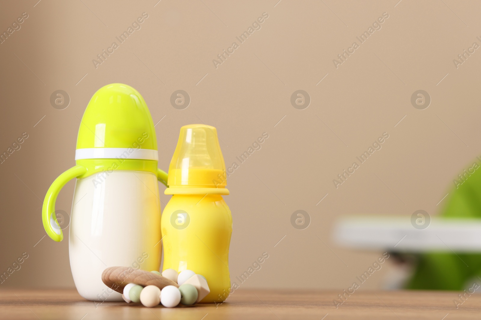 Photo of Feeding bottles with milk and toy on wooden table indoors, space for text