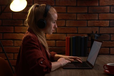 Photo of Woman in headphones working with laptop at table indoors