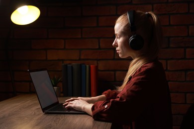 Photo of Woman in headphones working with laptop at table indoors