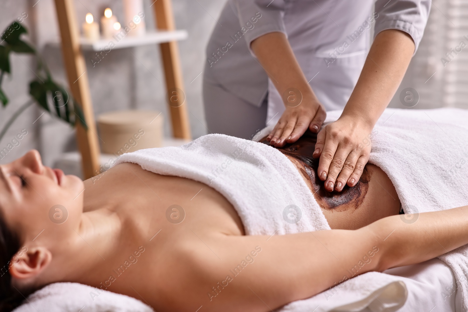 Photo of Woman undergoing chocolate body wrap treatment in spa salon, closeup