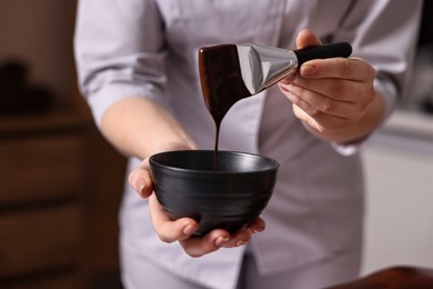 Photo of Spa worker with cosmetic product for chocolate body wrap in salon, closeup