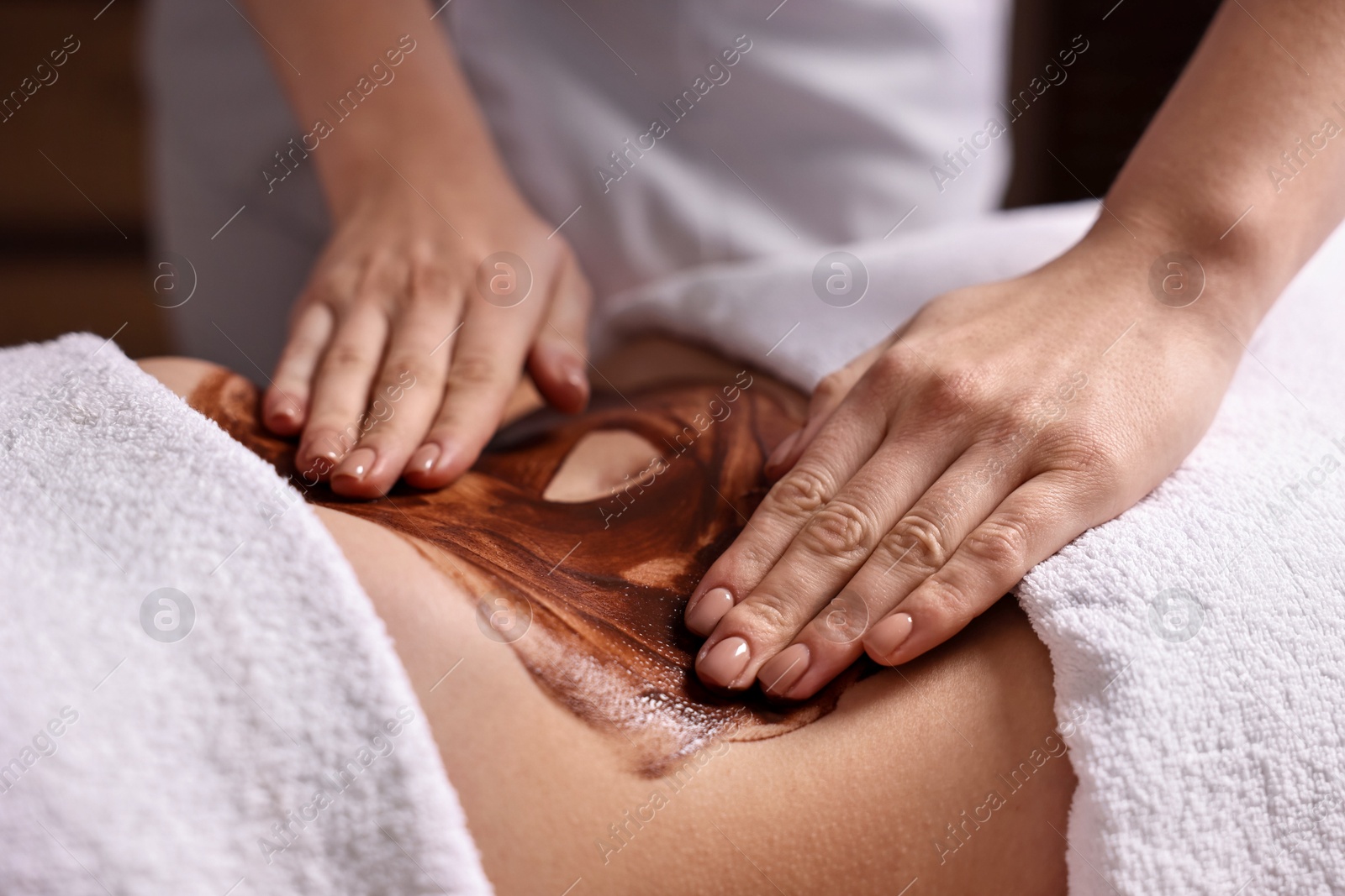 Photo of Woman undergoing chocolate body wrap treatment in spa salon, closeup