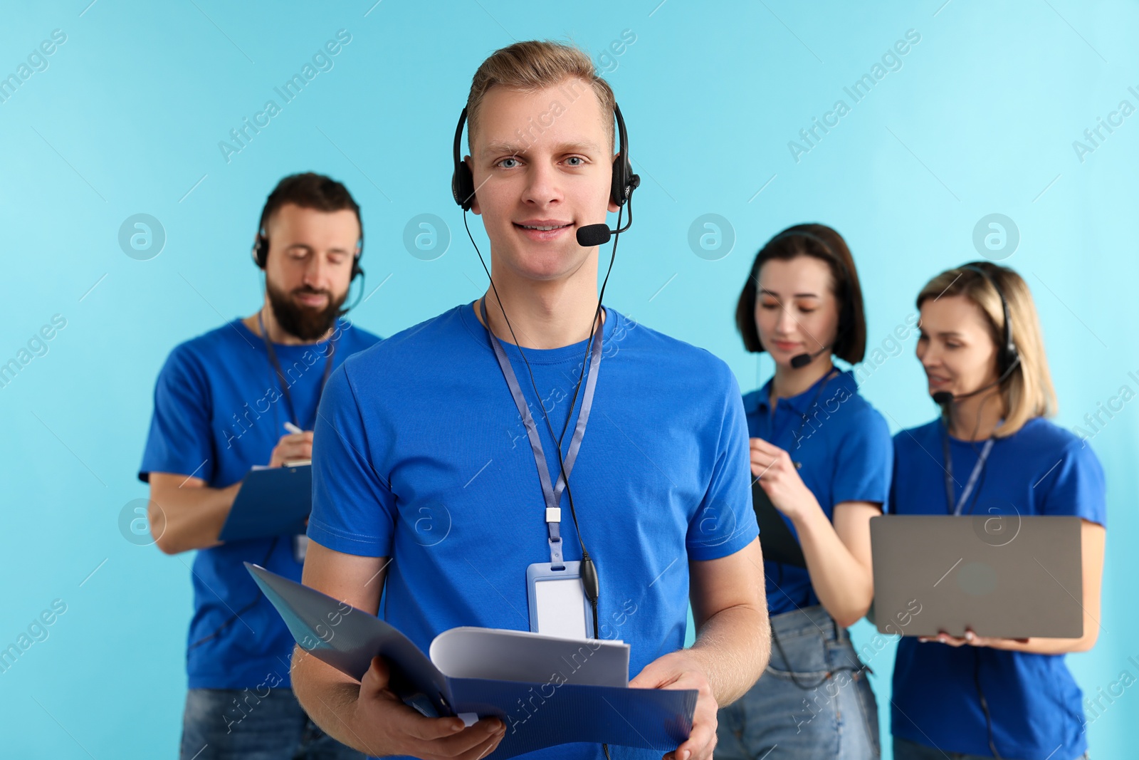 Photo of Technical support call center. Team of friendly operators working on light blue background