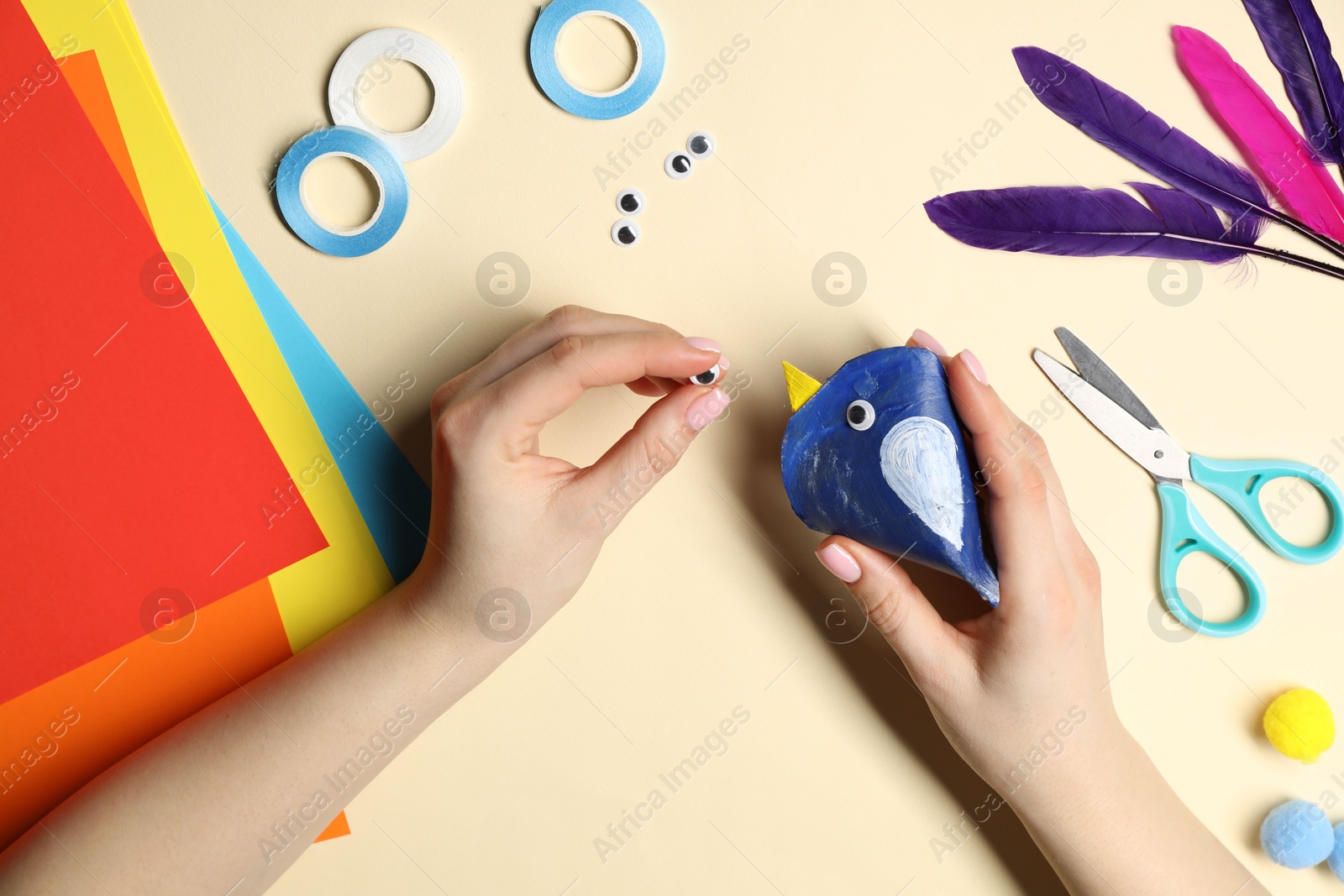 Photo of Woman making paper bird on pale yellow background, top view