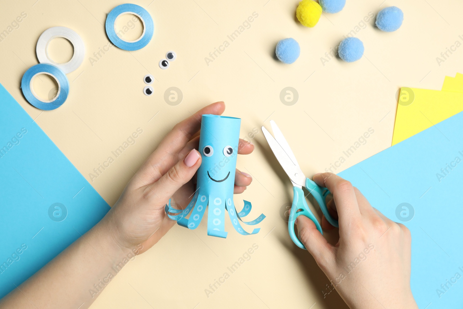 Photo of Woman making paper octopus on pale yellow background, top view