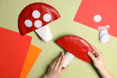 Photo of Woman making paper fly agaric on green background, top view