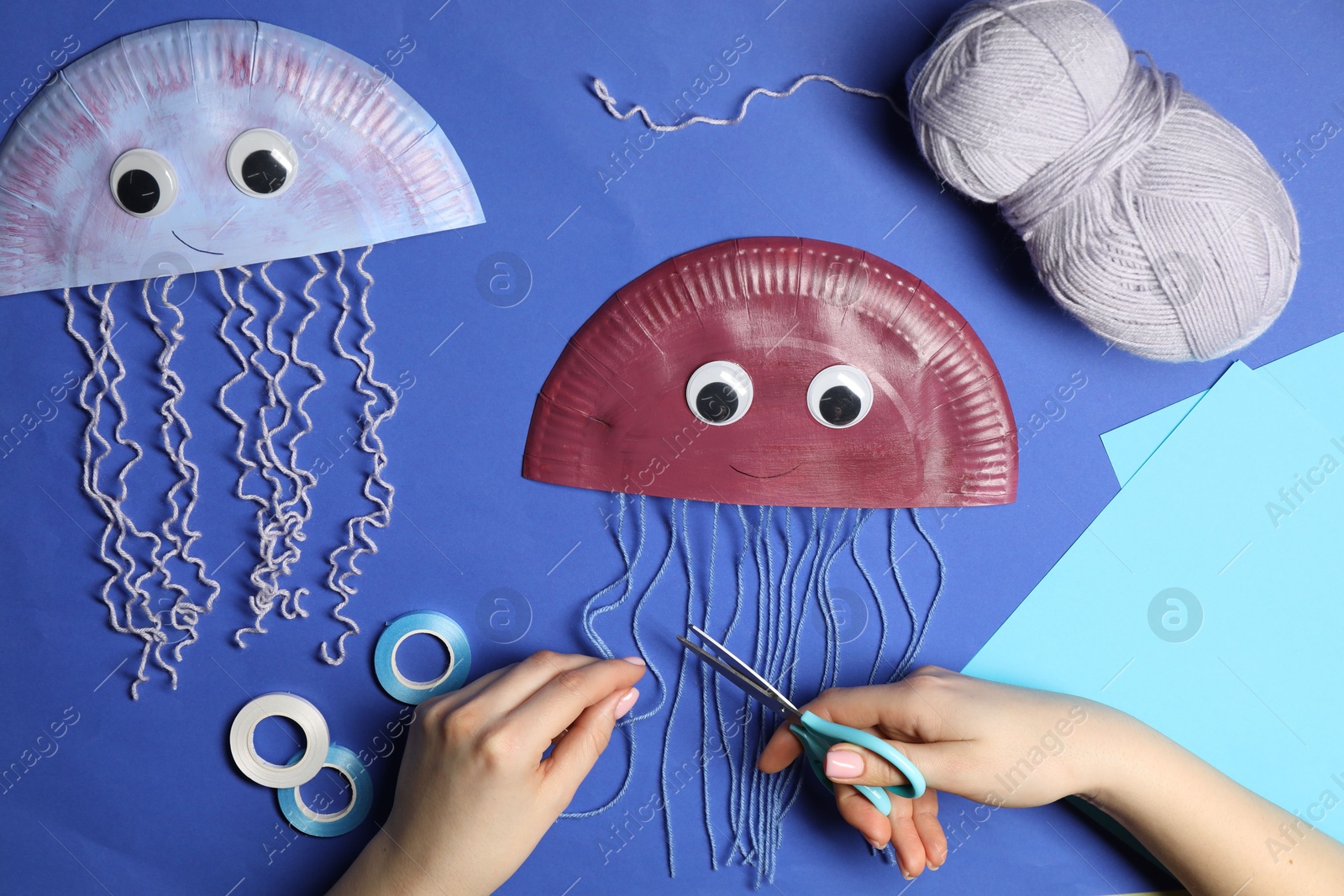 Photo of Woman making paper jellyfish on blue background, top view