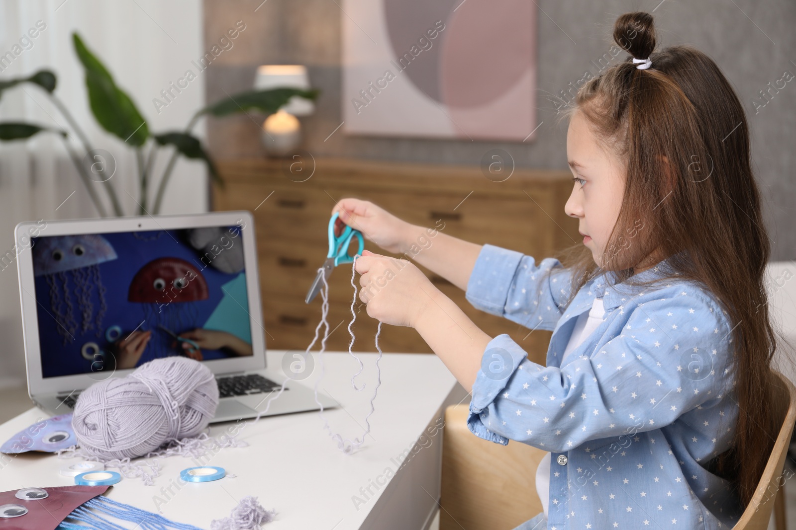 Photo of Little girl making handmade jellyfish by craft tutorial video at home. Child creativity