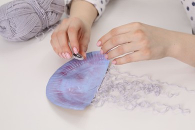 Photo of Woman making paper jellyfish at white table, closeup. Child handmade craft