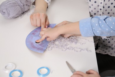 Photo of Woman and little girl making paper jellyfish at white table, closeup. Child handmade craft