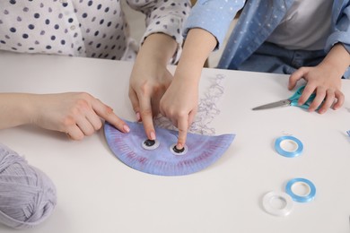 Photo of Woman and little girl making paper jellyfish at white table, closeup. Child handmade craft