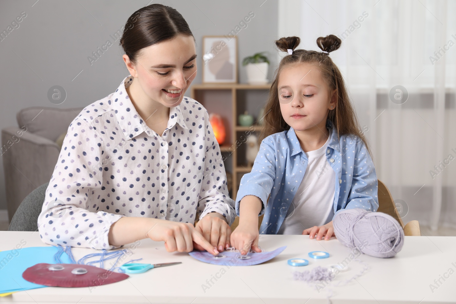 Photo of Woman and little girl making paper jellyfish at home. Child handmade craft