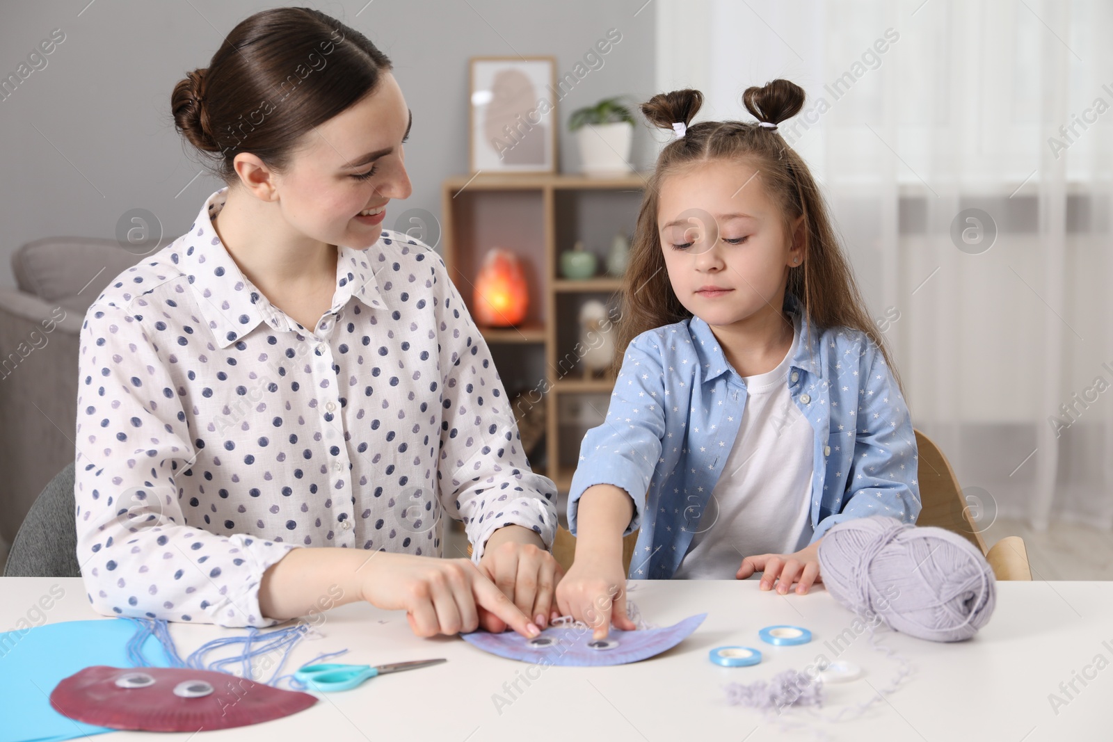 Photo of Woman and little girl making paper jellyfish at home. Child handmade craft