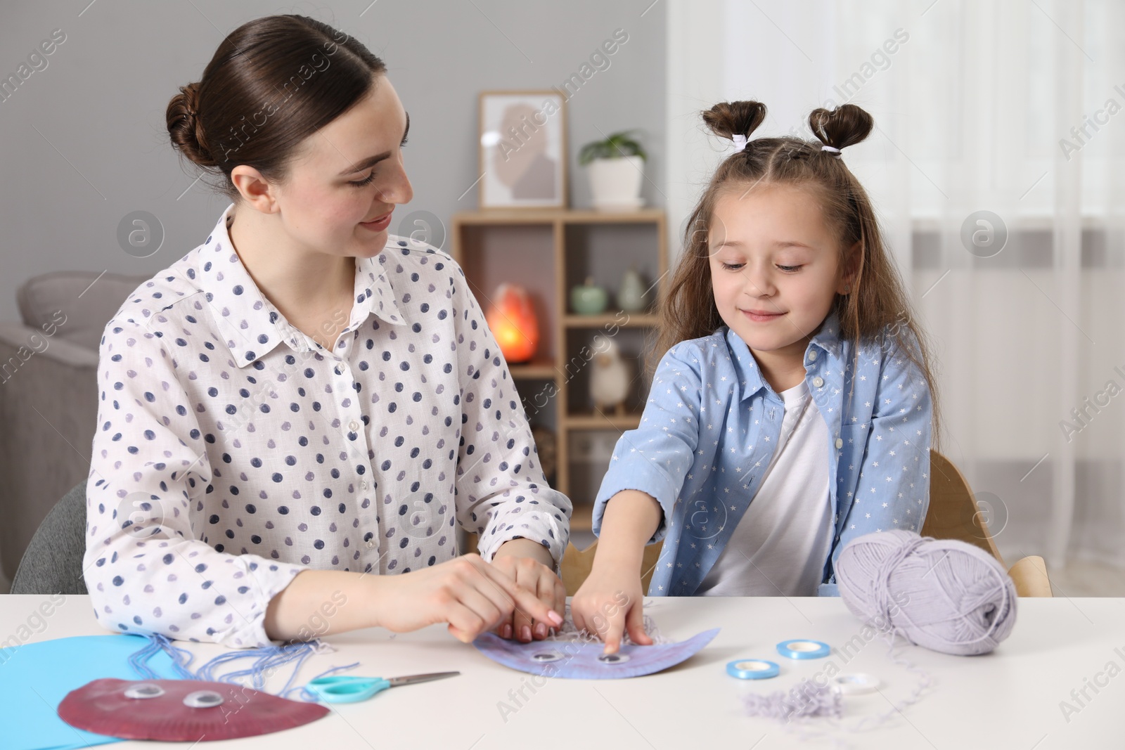 Photo of Woman and little girl making paper jellyfish at home. Child handmade craft