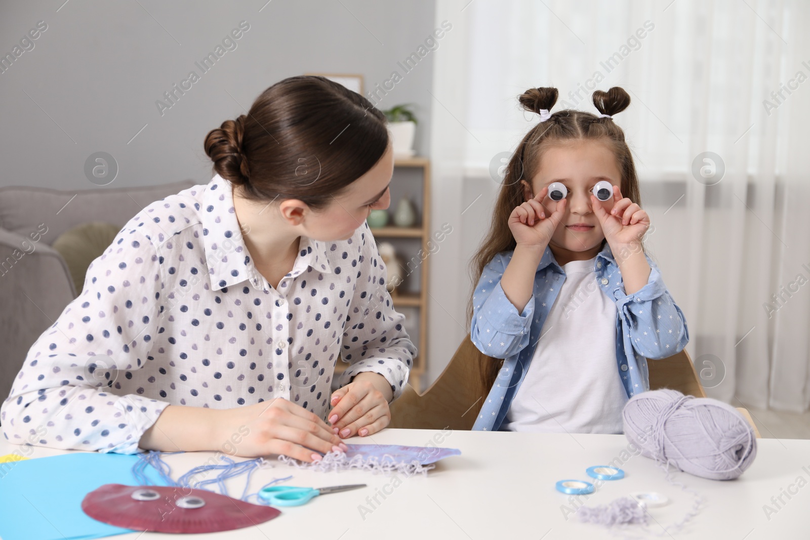 Photo of Woman and little girl having fun while making paper jellyfish at home. Child handmade craft