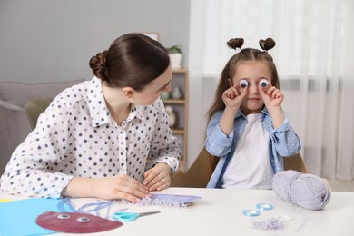 Woman and little girl having fun while making paper jellyfish at home. Child handmade craft