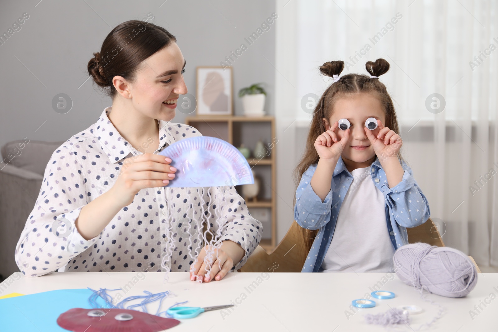 Photo of Woman and little girl having fun while making paper jellyfish at home. Child handmade craft