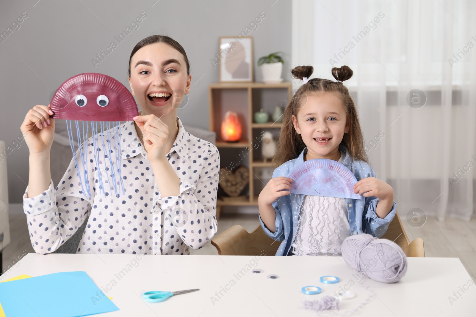 Photo of Woman and little girl with paper jellyfish at white table indoors. Child creativity