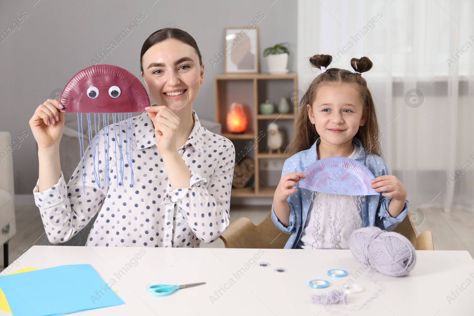 Photo of Woman and little girl with paper jellyfish at white table indoors. Child creativity