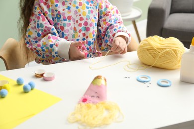 Photo of Little girl making craft at white table indoors, closeup. Child creativity